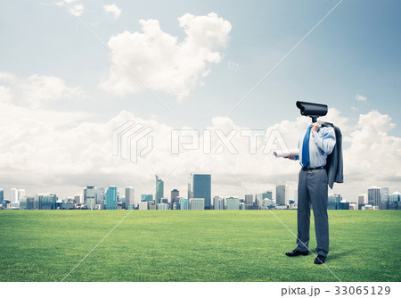 Camera headed man standing on green grass against modern citysca Camera headed man standing on green grass against modern citysca 33065129