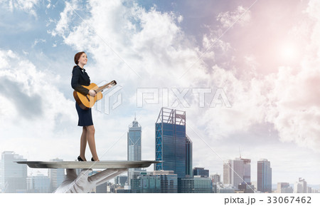 Attractive businesswoman on metal tray playing acoustic guitar against cityscape background Attractive businesswoman on metal tray playing acoustic guitar against cityscape background 33067462