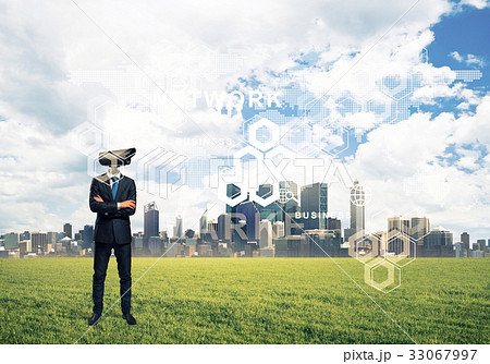 Camera headed man standing on green grass against modern citysca Camera headed man standing on green grass against modern citysca 33067997