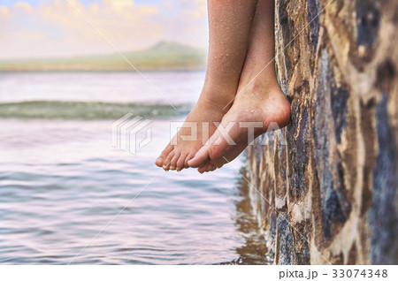 Young girl's feet dangling from the stone jetty Young girl's feet dangling from the stone jetty 33074348