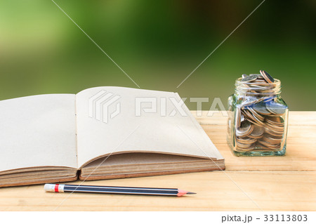 Book and Coin in glass jar on wooden table 33113803
