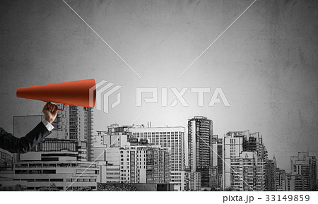 Hand of businesswoman holding red paper trumpet against cityscape background Hand of businesswoman holding red paper trumpet against cityscape background 33149859