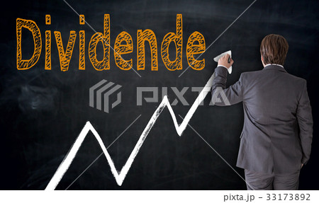 Businessman writes Dividende (in german dividend) on blackboard 33173892
