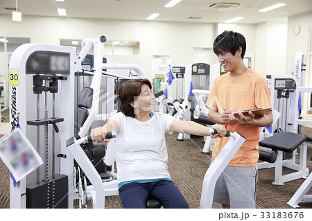 スポーツクラブでマシーントレーニングをアドバイスもらう高齢者女性 33183676