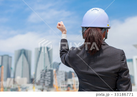 工事現場に向かってガッツポーズをする ヘルメットをかぶったスーツ姿の女性 後姿の写真素材