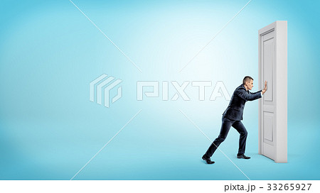 A small businessman pushes a closed door on a 33265927