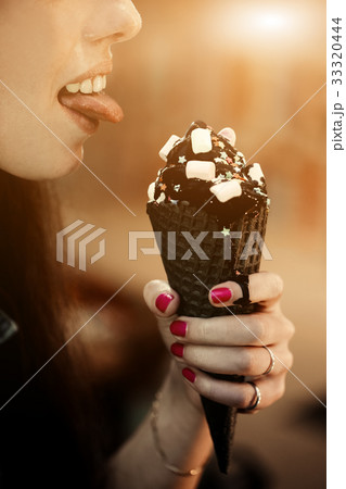 Woman licks trend cone of charcoal ice cream with Woman licks trend cone of charcoal ice cream with 33320444