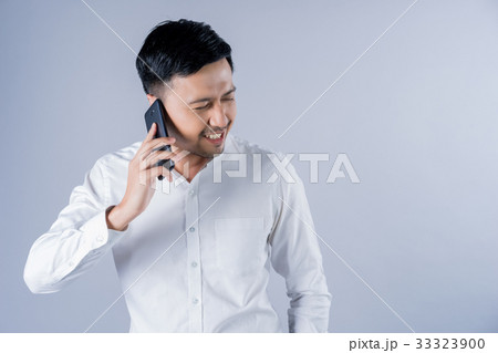 The asian man in white shirt is talking on the phone on gray background The asian man in white shirt is talking on the phone on gray background 33323900