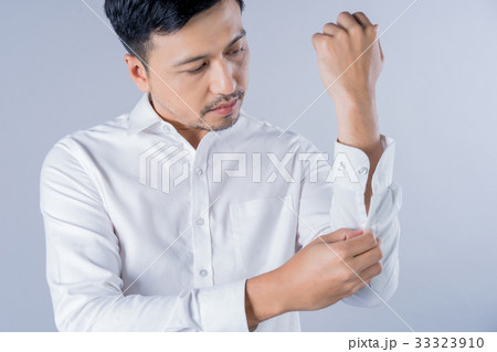 A man is fastening the buttons of his white shirt 33323910