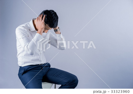 a businessman is sitting and holding his head on gray background a businessman is sitting and holding his head on gray background 33323960