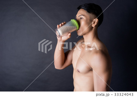 Asian body builder is drinking a protein shake on black background 33324043