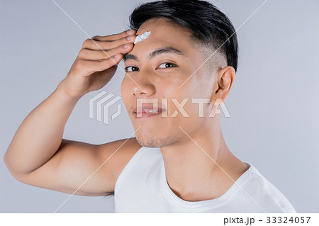 Young man is applying cleansing cream on his forehead 33324057