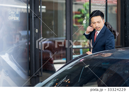 A businessman is carrying his bag over his shoulder and looking at the car. A businessman is carrying his bag over his shoulder and looking at the car. 33324229