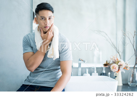 A handsome man is touching his chin and looking at the camera in the bathroom. 33324262