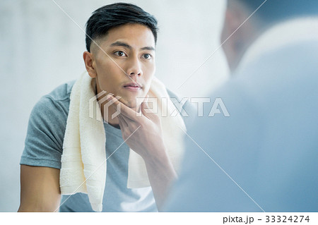 a picture of a man looking at the mirror and touching his chin in the bathroom a picture of a man looking at the mirror and touching his chin in the bathroom 33324274