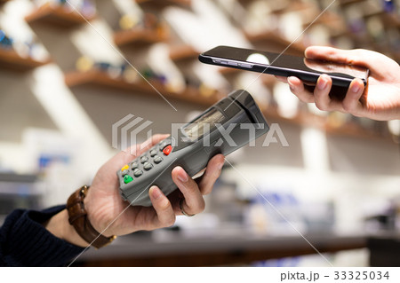 Woman paying with NFC technology on mobile phone in shop Woman paying with NFC technology on mobile phone in shop 33325034