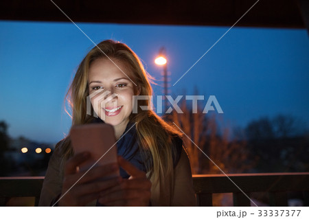 Woman in the city at night holding smartphone Woman in the city at night holding smartphone 33337377