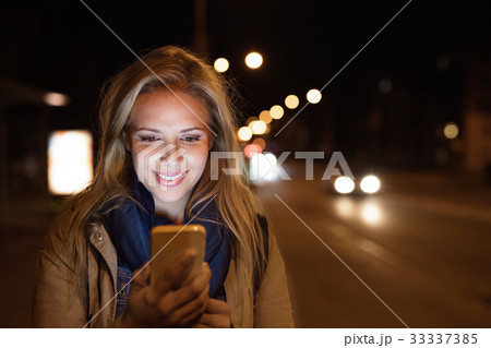 Woman in the city at night holding smartphone Woman in the city at night holding smartphone 33337385