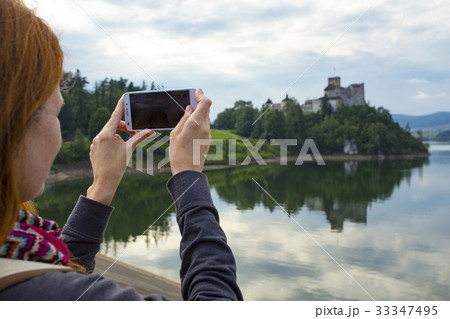 girl taking a picture of a beautiful castle on a lake shore 33347495