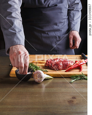 Chef seasoning rib eye steak on wooden board at 33349807