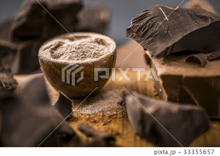 Ground chocolate in wooden bowl next to chunk of chocolate 33355657