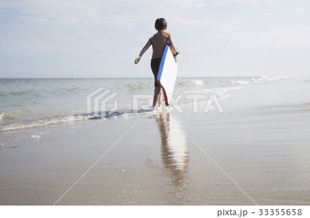 Boy (8-9) walking and carrying body board in empty beach 33355658
