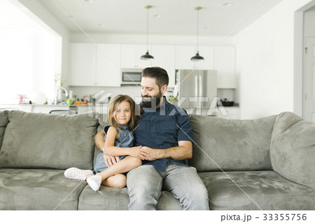 Father with daughter (6-7) sitting on sofa in living room 33355756