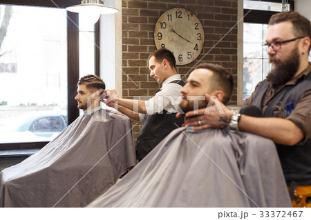 Man getting haircut by hairstylist at barbershop 33372467