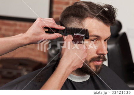 The hands of barber making haircut to young man in The hands of barber making haircut to young man in 33421539