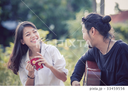 younger asian man and woman relaxing playing guitar in park 33459556