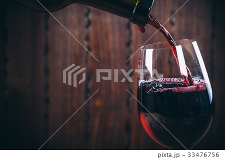 Pouring red wine into the glass against wooden Pouring red wine into the glass against wooden 33476756