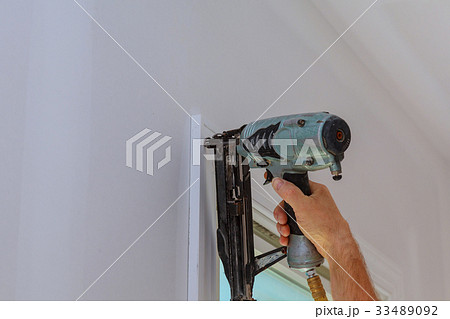 Carpenter using nail gun to moldings on windows 33489092