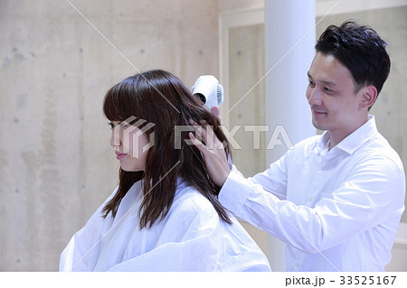 美容室でヘアスタイリストに髪を乾かしてもらう女性の写真素材