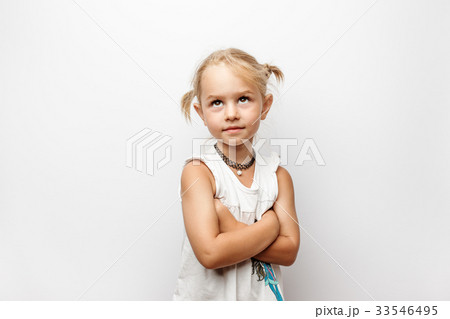 Little girl in white dress with crossed arms looks 33546495