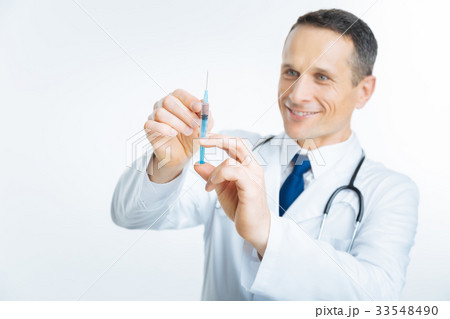 Radiant mature doctor looking at syringe 33548490