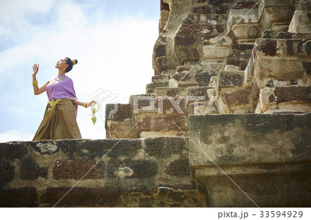 A woman in Thai dress is looking sky and raising her hand at a temple 33594929