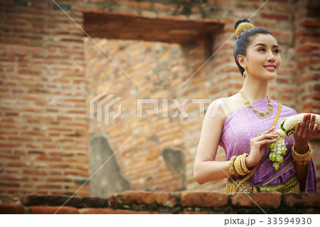 A Thai woman is holding a garland and smiling at a temple 33594930