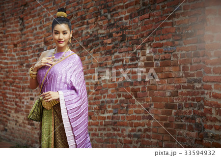 A woman in Thai dress is standing near by a brick wall A woman in Thai dress is standing near by a brick wall 33594932