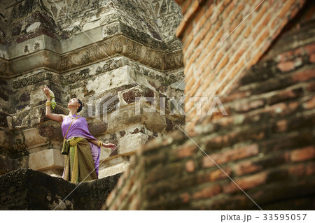 a thai woman is dancing in traditional costume at a temple 33595057