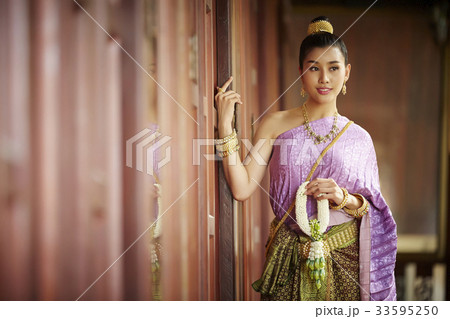 A beautiful Thai woman is glancing at something while leaning on the door. 33595250