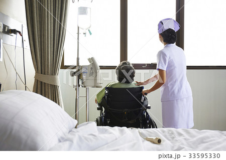 The nurse and the elderly patient are looking outside from glass window 33595330