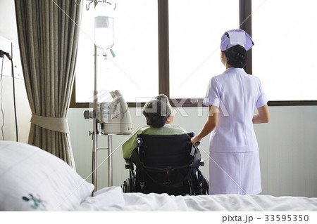 A nurse and an old patient are looking outdoor from the window 33595350