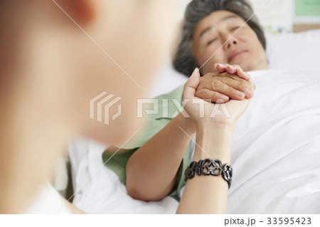elderly woman is lying down in bed and holding someone's hand elderly woman is lying down in bed and holding someone's hand 33595423