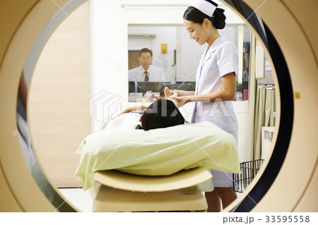 A photo of an Asian young nurse helping a patient while a doctor is looking through the glass. A photo of an Asian young nurse helping a patient while a doctor is looking through the glass. 33595558