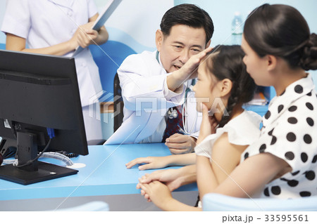 An Asian doctor is touching a little girl 's head for doing a health examination. An Asian doctor is touching a little girl 's head for doing a health examination. 33595561