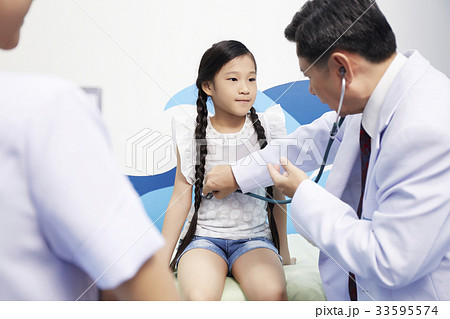 The little girl is looking at the doctor while he is doing a physical examination. The little girl is looking at the doctor while he is doing a physical examination. 33595574