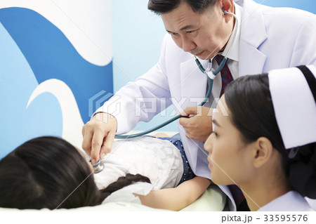 An Asian young nurse is looking at the patient while a doctor is doing an examination. 33595576