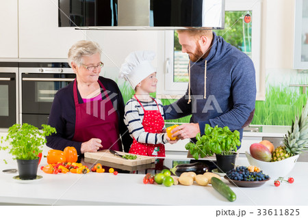 Dad, grandma and kid cooking together in kitchen 33611825