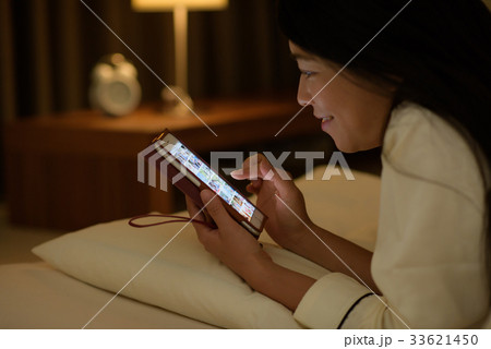 ベッドでスマホを見る女性の写真素材 ベッドでスマホを見る女性の写真素材