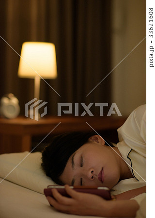 布団の中でスマホを見る女性 33621608